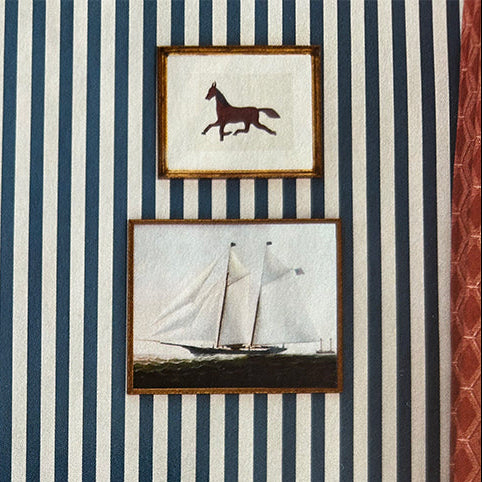 Navy and white striped wallpaper with vintage framed pictures in a room with wooden furniture and a wicker basket.