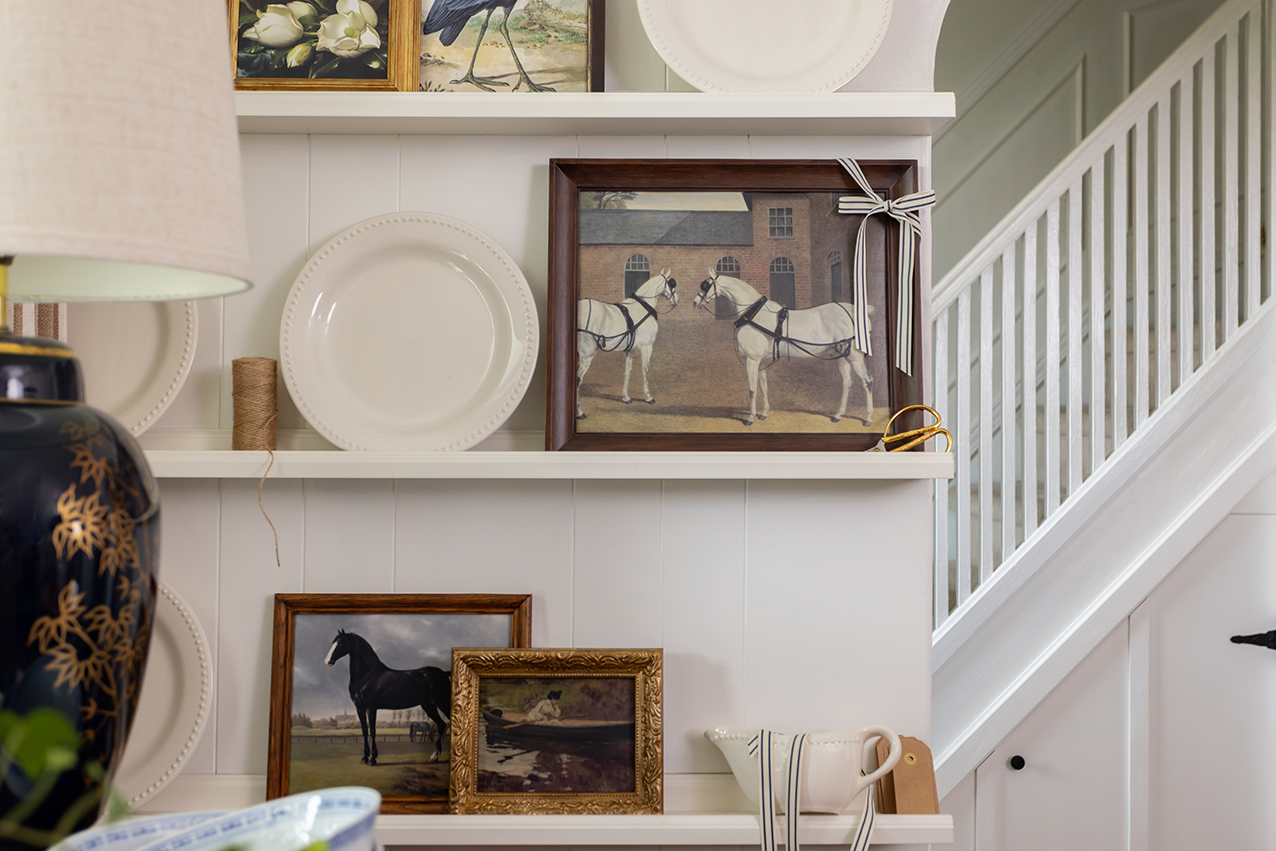 Decorative shelf with framed pictures of horses and other items against a white wall.