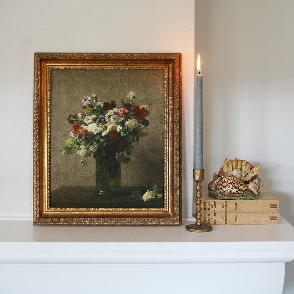 Framed painting of flowers on a shelf with a candle and decorative items.