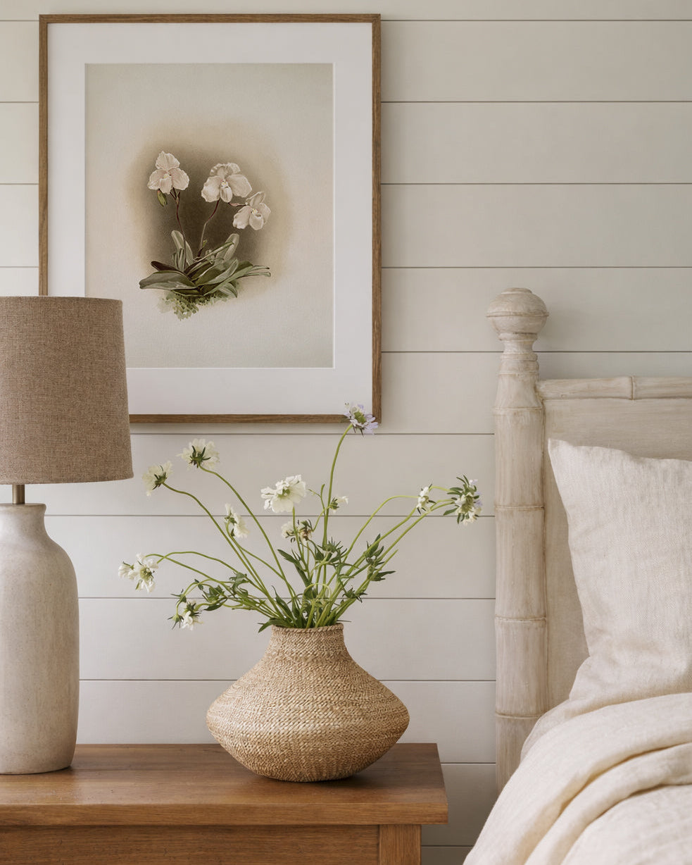 Bedroom with wooden nightstand, lamp, and framed vintage Orchid artwork on a white wall.
