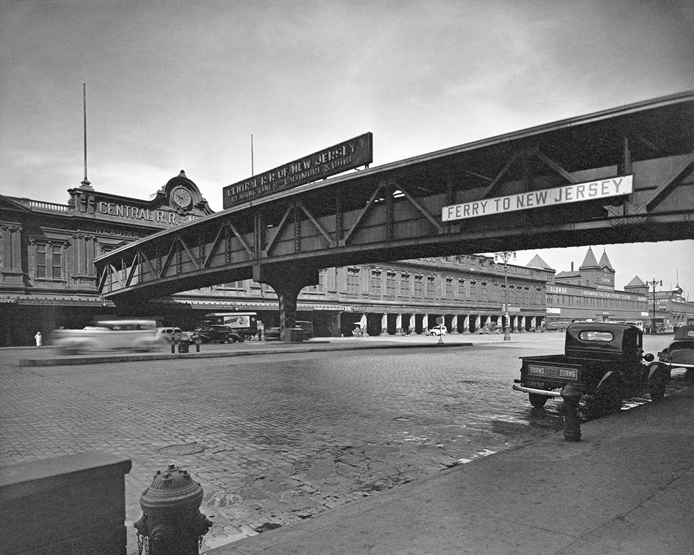 Vintage black and white photo of a street scene with a ferry sign over a road.