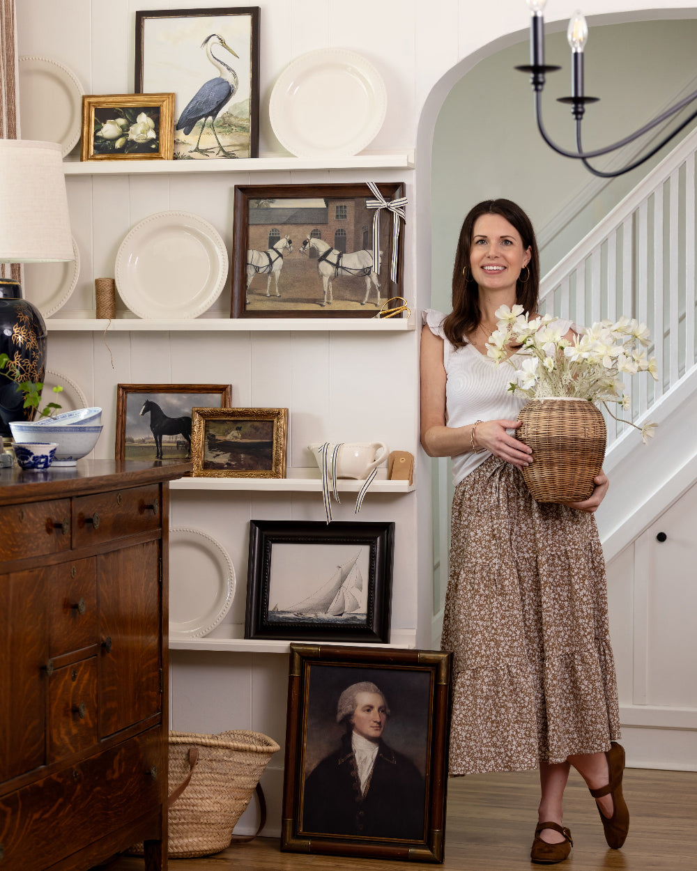 Woman holding a basket of flowers in a room with decorative items on shelves.